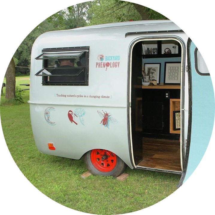 Photo of a silver camper with an open door, located in a park setting with green grass.